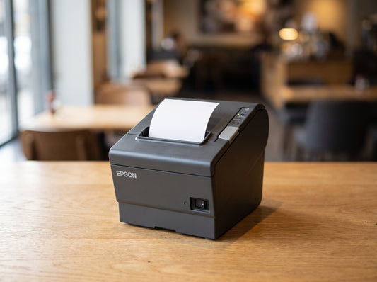 Epson TM-T88V thermal receipt printer in Epson Dark Gray on a cafe counter, receipt paper loaded — AI-generated image