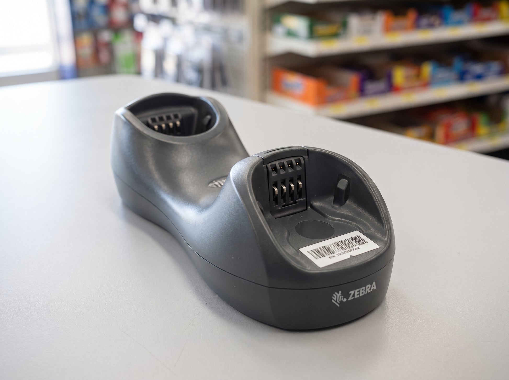 Zebra CR0078 standard base charging and communication cradle in Twilight Black, shown empty on a pharmacy counter — cradle only, scanner not included