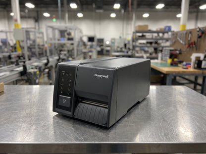 Honeywell PM45c compact industrial thermal transfer label printer on a stainless steel workbench in a production area
