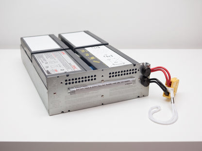 APC APCRBC133 replacement battery cartridge on a white service bench, galvanised tray with yellow connector — AI-generated image