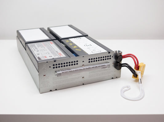 APC APCRBC133 replacement battery cartridge on a white service bench, galvanised tray with yellow connector — AI-generated image