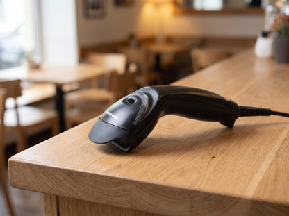Honeywell MS5145 Eclipse single-line 1D laser barcode scanner in black with its USB cable, on a cafe counter — AI-generated image