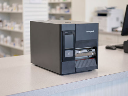 Honeywell PD45S industrial thermal transfer label printer in black with colour touch display on a pharmacy counter — AI-generated image