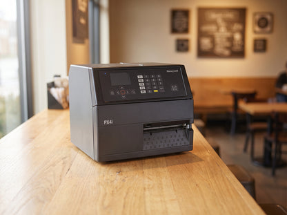 Honeywell PX4ie industrial thermal transfer label printer in black on a wooden cafe counter — AI-generated image