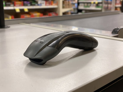 Honeywell Voyager 1200g corded 1D laser barcode scanner in black on a retail checkout counter — AI-generated image