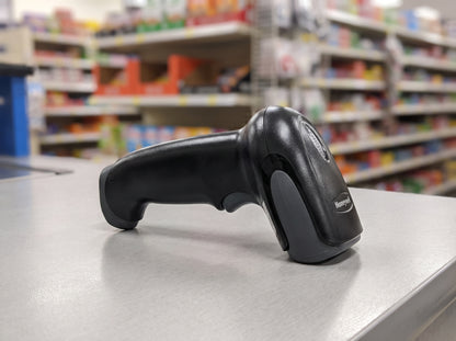 Honeywell Voyager 1250g corded 1D laser barcode scanner in black on a retail checkout counter — AI-generated image