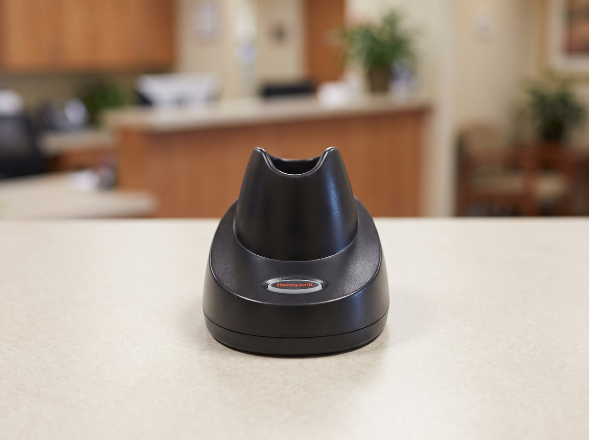 Honeywell CCB10 charging and communication base in black, shown empty on a cafe counter — AI-generated image