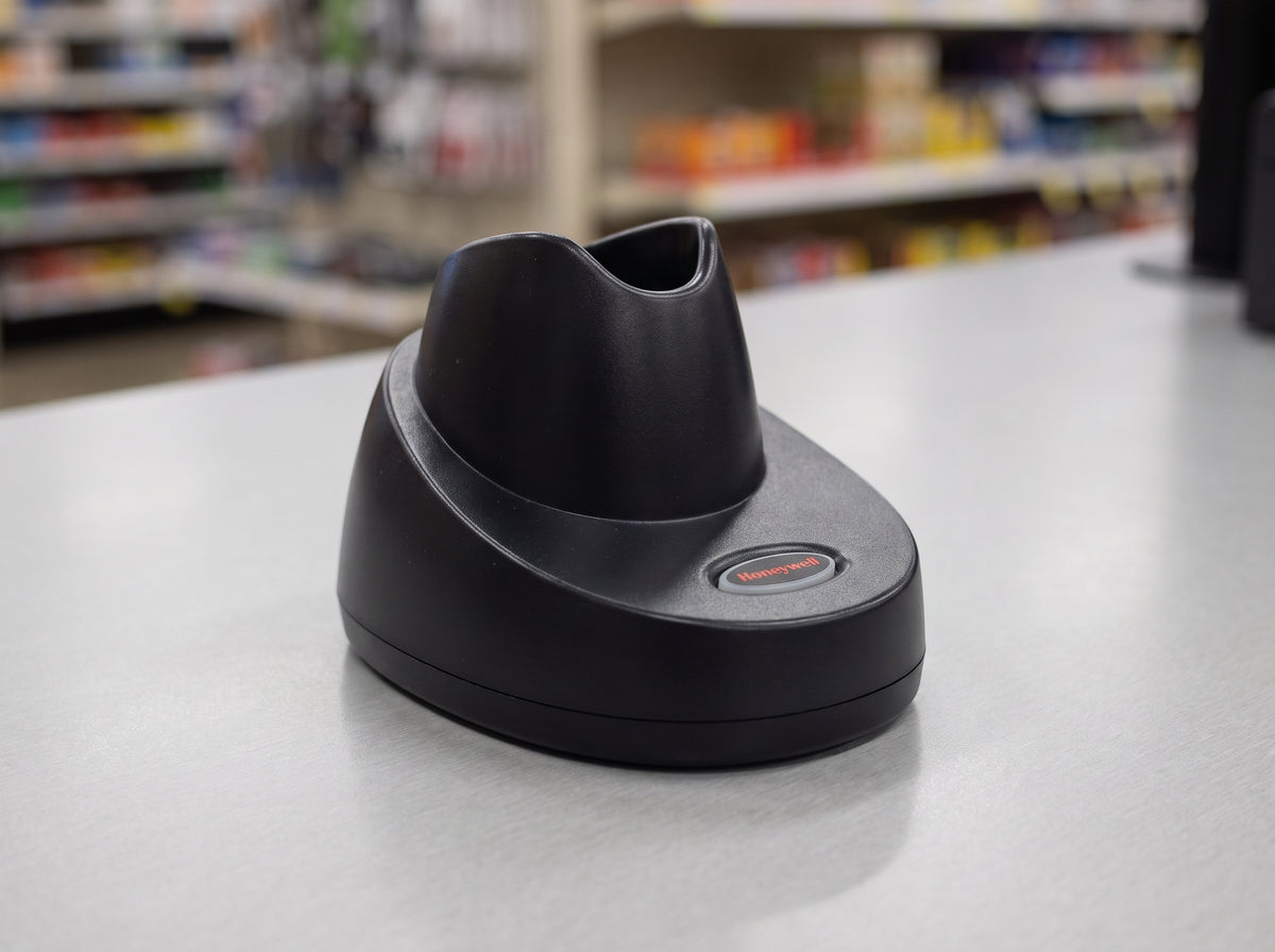 Honeywell CCB10 charging and communication base in black, shown empty on a pharmacy counter — AI-generated image