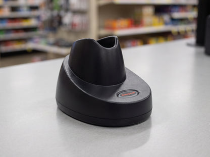 Honeywell CCB10 charging and communication base in black, shown empty on a pharmacy counter — AI-generated image