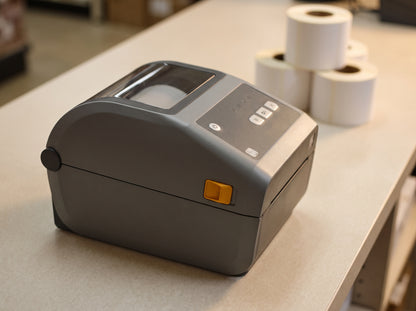 Zebra ZD621 300 dpi direct thermal desktop label printer on a back-office counter with blank label rolls behind — AI-generated image